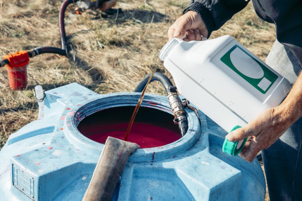 men's hands pouring a chemical into a large blue plastic tank filled, agricultural mixing process, hoses connected for chemical transfer in sunny rural field, agriculture, irrigation, chemistry, fungicides